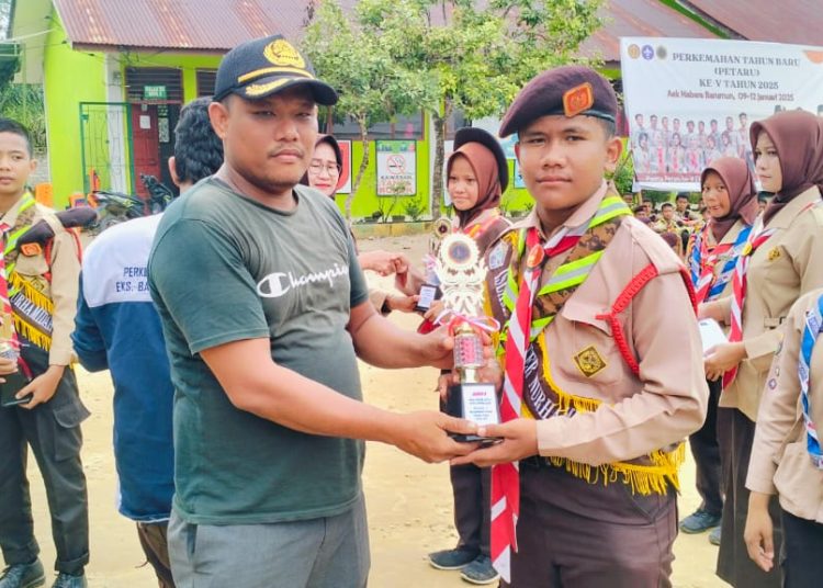 Paujan Munawir,  Guru MTsN 2 Padang Lawas (kiri) saat menyerahkan trophy kepada Pramuka Penggalang yang keluar sebagai pemenang pada Perkemahan Tahun Baru 2025.(Satunusantara news/HO-Humas Kemenag Sumut).