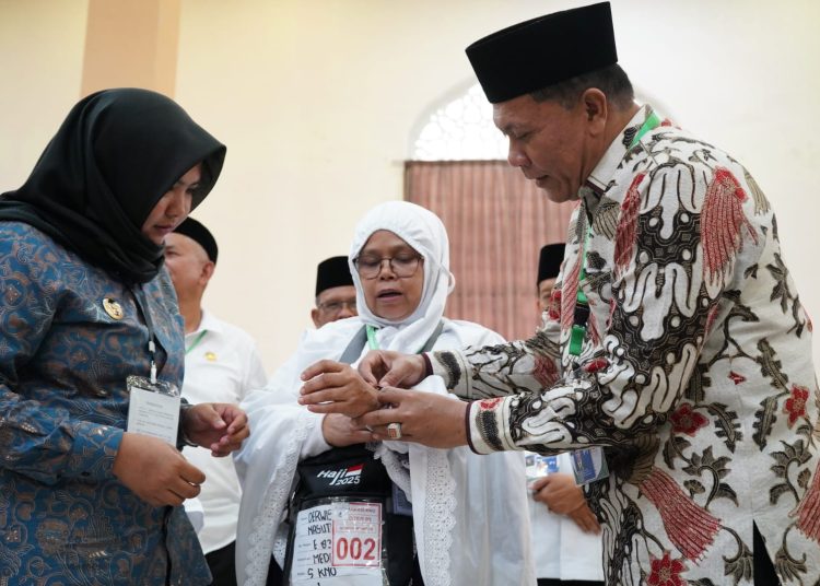 Ketua PPIH Embarkasi Medan, H. Ahmad Qosbi (kanan) disaksikan oleh Wakil Bupati  Madina, Atika Azmi Utammi Nasution (kiri) memasangkan gelang kepada salah seorang jemaah haji Kloter 05 asal Kabupaten Madina.(Satunusantara news/HO-Humas PPIH Embarkasi Medan).