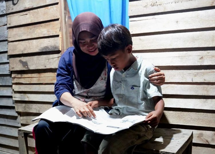 Wiwik Handayani, warga Sungai Kunyit , Mempawah,Kalimantan Barat sedang menemani anaknya belajar di rumah pada malam hari pascadirinya menerima bantuan penyambungan listrik gratis melalui progra Light Up The Dream PLN.(Satunusantara news/HO-Humas PLN UID Sumut)